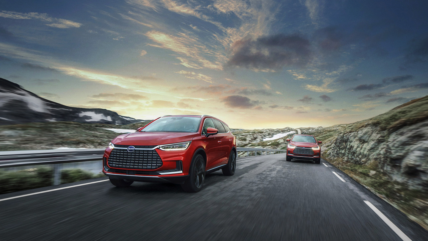 To røde elektriske BYD biler kører på en vej 